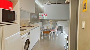 Une cuisine compacte équipée d’un four à micro-ondes, d’un lave-linge et d’un petit coin repas avec des chaises et une table.