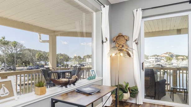 En balkon med udsigt over en lysthavn, en fletstol, et bord med en bog og en gulvlampe.