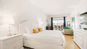 A hotel room with a large bed, a desk with a lamp, a dresser, and a view of the outside. - Harbor View Charm, King Bed, Balcony (St. Augustine)