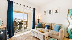 A cozy living room with a sofa, a coffee table, and a view of a marina through a glass door. - Harbor View Charm, King Bed, Balcony (St. Augustine)