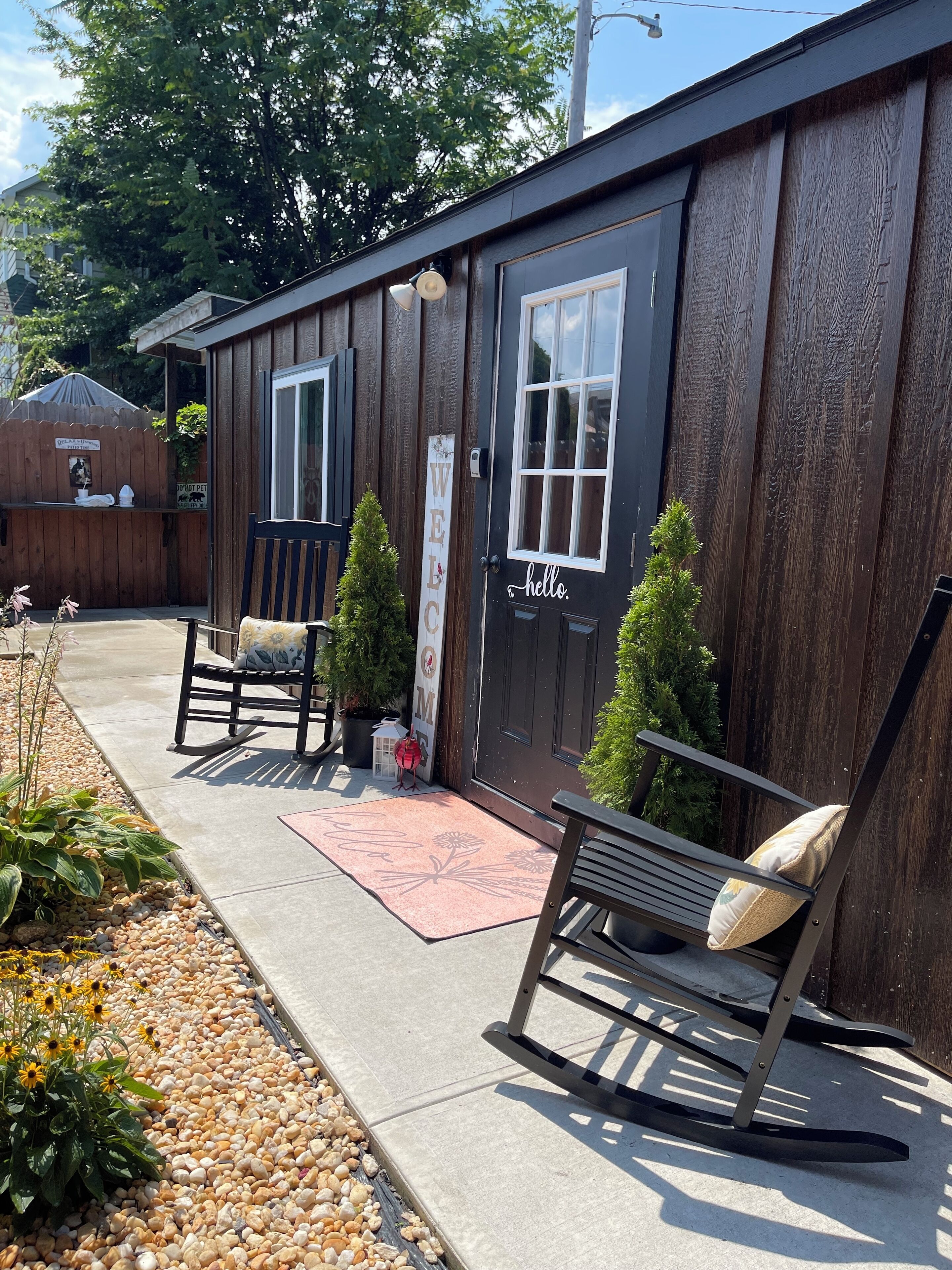 A wooden building with a 'WELCOME' sign, a bench, a rocking chair, and a small potted plant.