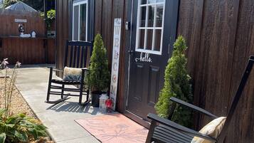 A wooden building with a 'WELCOME' sign, a bench, a rocking chair, and a small potted plant.