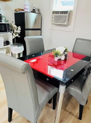 Un coin repas avec une table en verre rouge, des chaises à revêtement gris et une poubelle en acier inoxydable.
