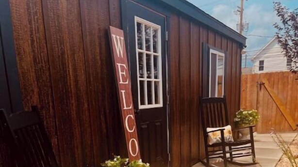 A wooden building with a 'WELCOME' sign, two rocking chairs with cushions, and a small garden area with pebbles and plants. - Cabin Experience near all (Wilkes-Barre)