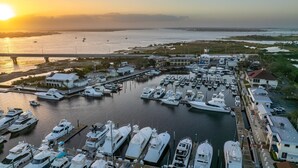A marina with multiple boats docked, a bridge in the background, and buildings along the waterfront.