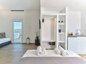 Moderni hotellihuone, jossa on sänky, merinäköala, pieni parveke, minikeittiö ja kylpyhuone.