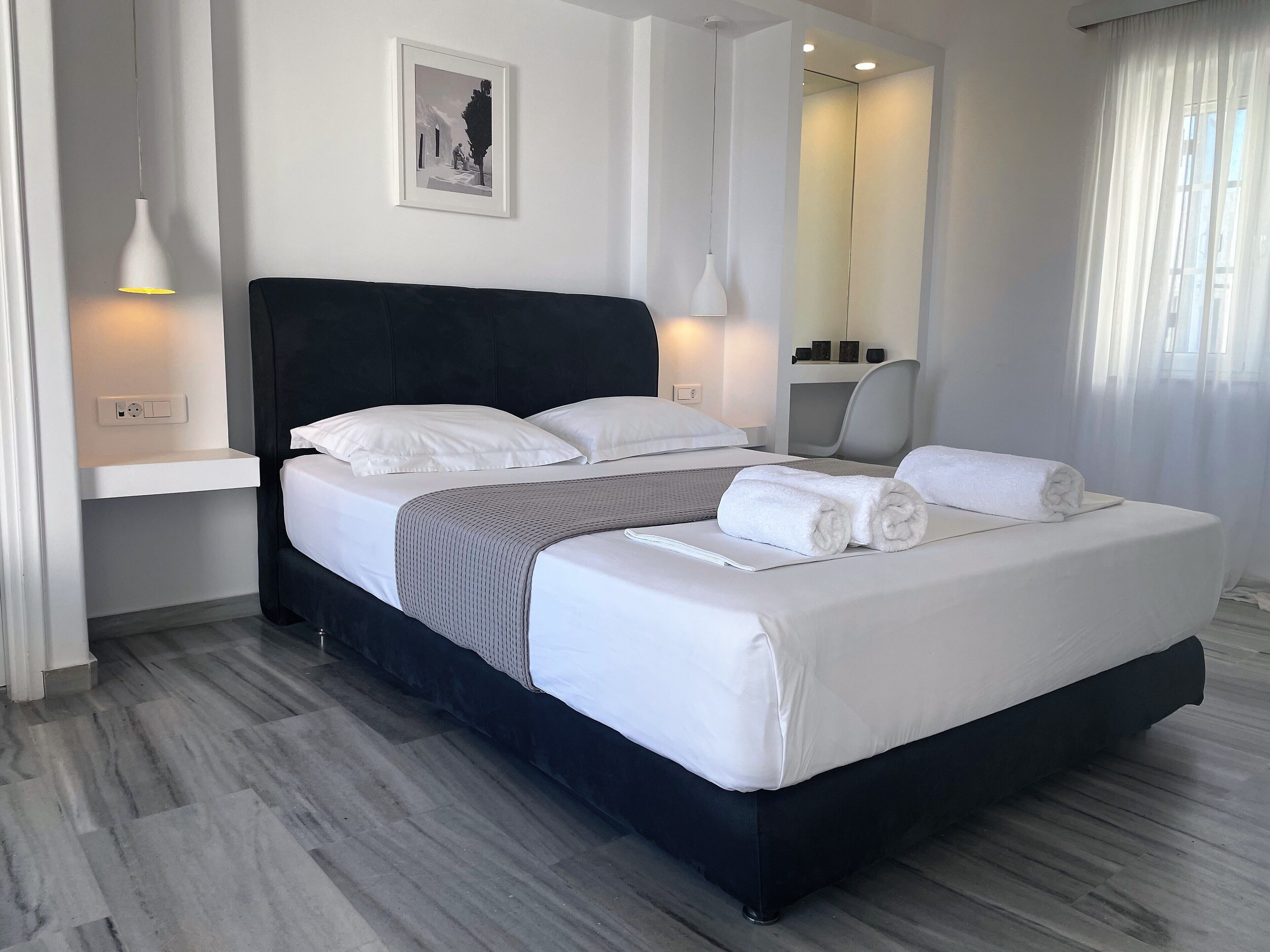 A modern hotel room with a large bed, bedside lamps, a framed picture on the wall, and a mirror above the bed.