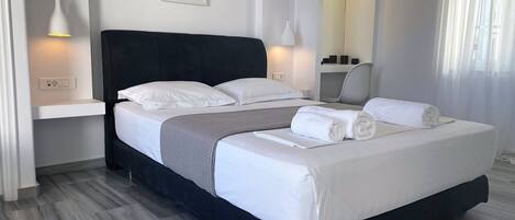 A modern hotel room with a large bed, bedside lamps, a framed picture on the wall, and a mirror above the bed.