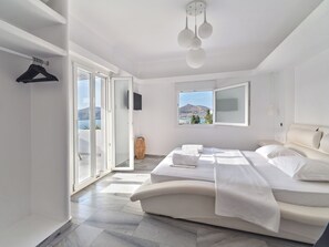 A modern bedroom with a large bed, a view of the sea, and a sliding glass door leading to an outdoor area. - Villa Irini (Paros)