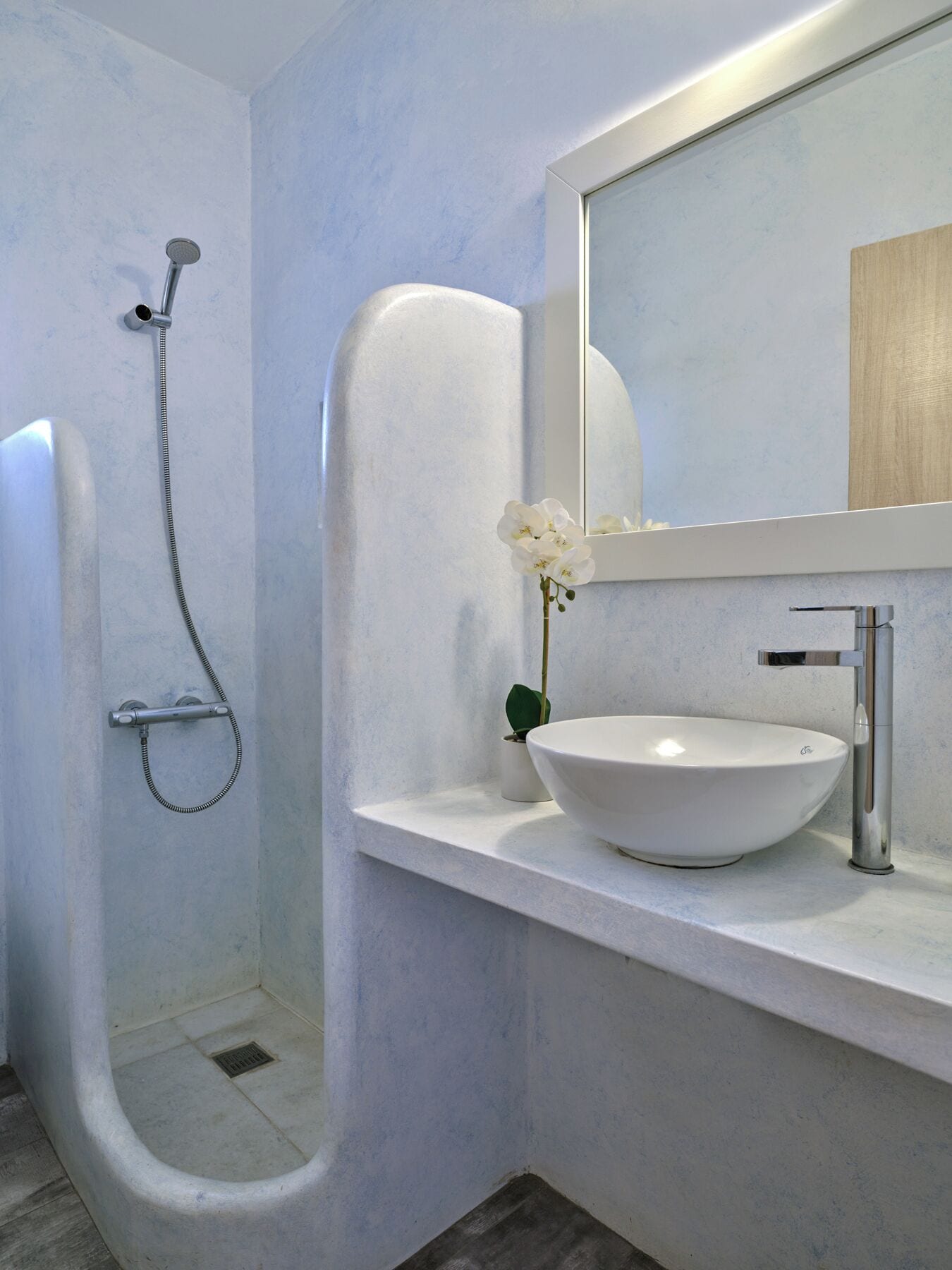 A modern bathroom with a walk-in shower, a white sink, and a mirror with a wooden frame.