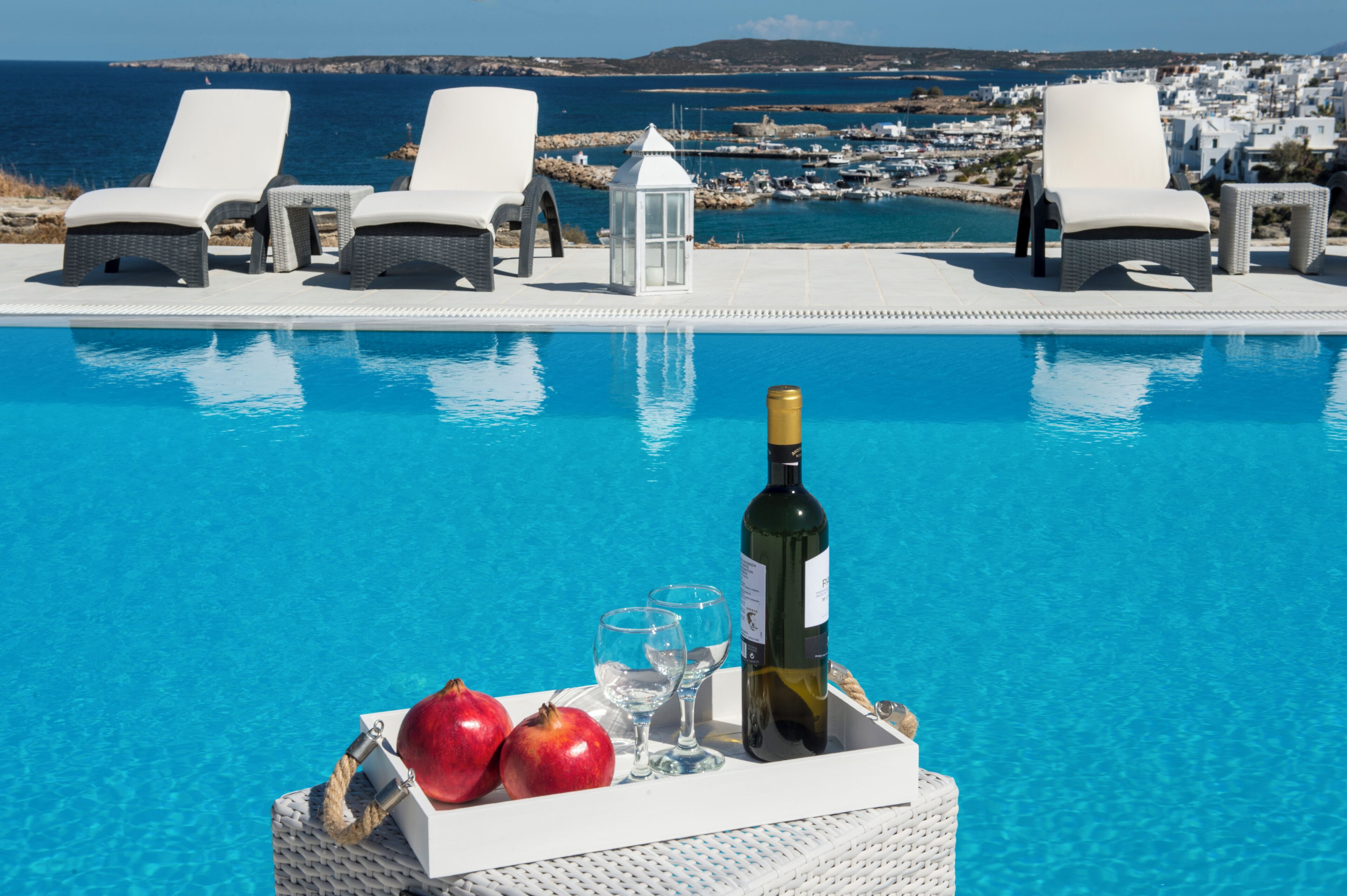 A poolside area with lounge chairs, a bottle of wine, and two glasses on a tray.