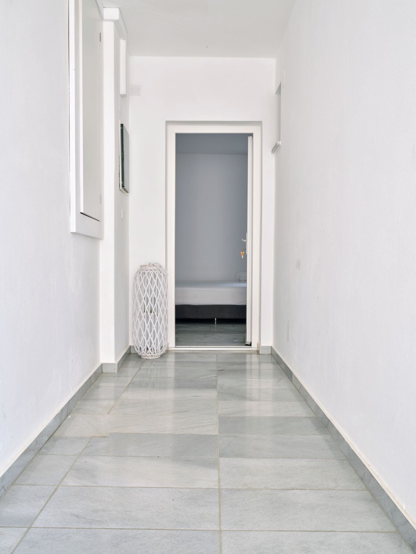 A narrow hallway with a tiled floor, a white door at the end, and a small trash bin to the left.
