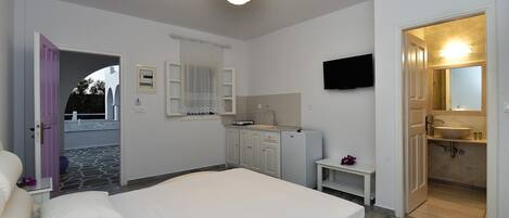 A bedroom with a bed, a small bedside table, a mirror, a TV mounted on the wall, and a bathroom with a sink and mirror.