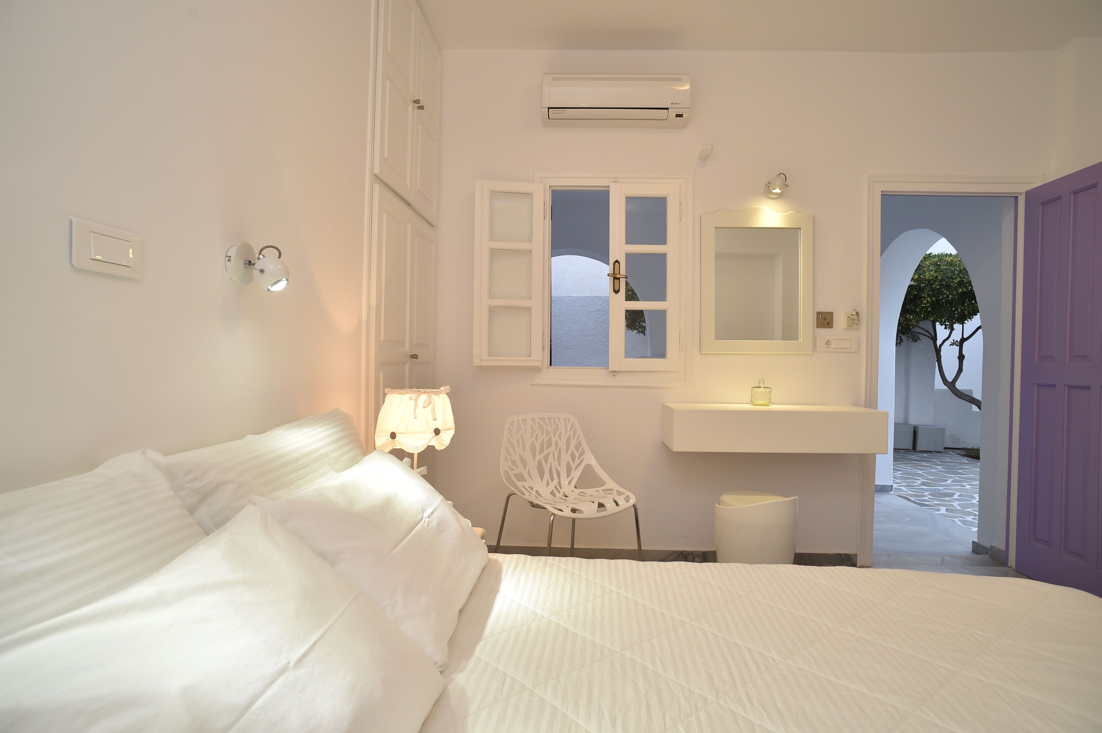 Un dormitorio con cama, una silla, tocador con espejo y ventana con vista al mar.