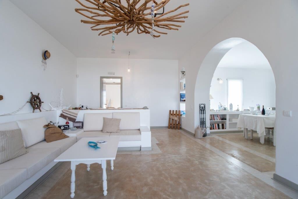 Un soggiorno moderno con un divano bianco, un tavolino da caffè, un lampadario di legno originale e una cucina visibile tramite un arco.