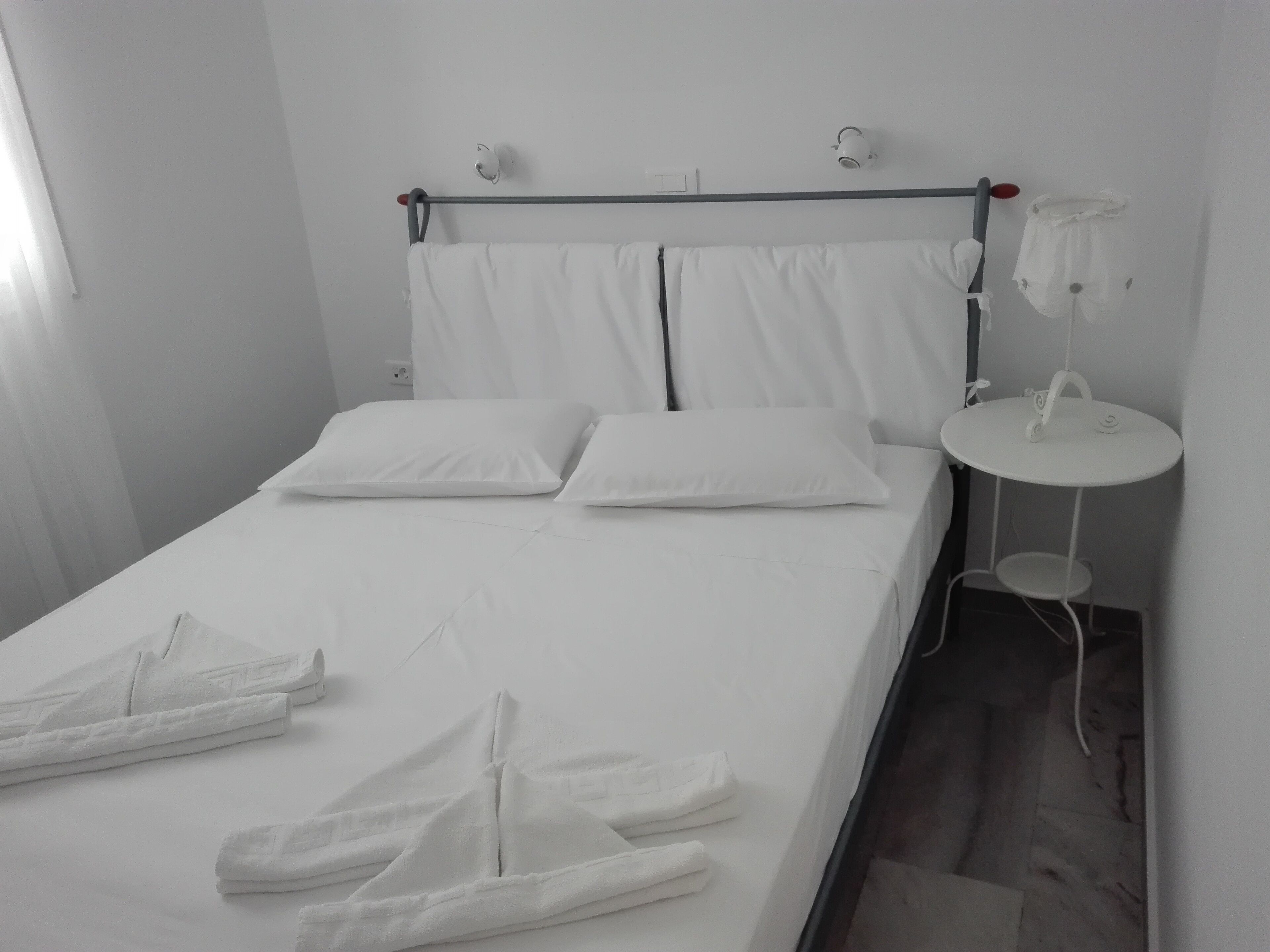 A single bed with white linens, a bedside table with a lamp, and a small round table with a chair.
