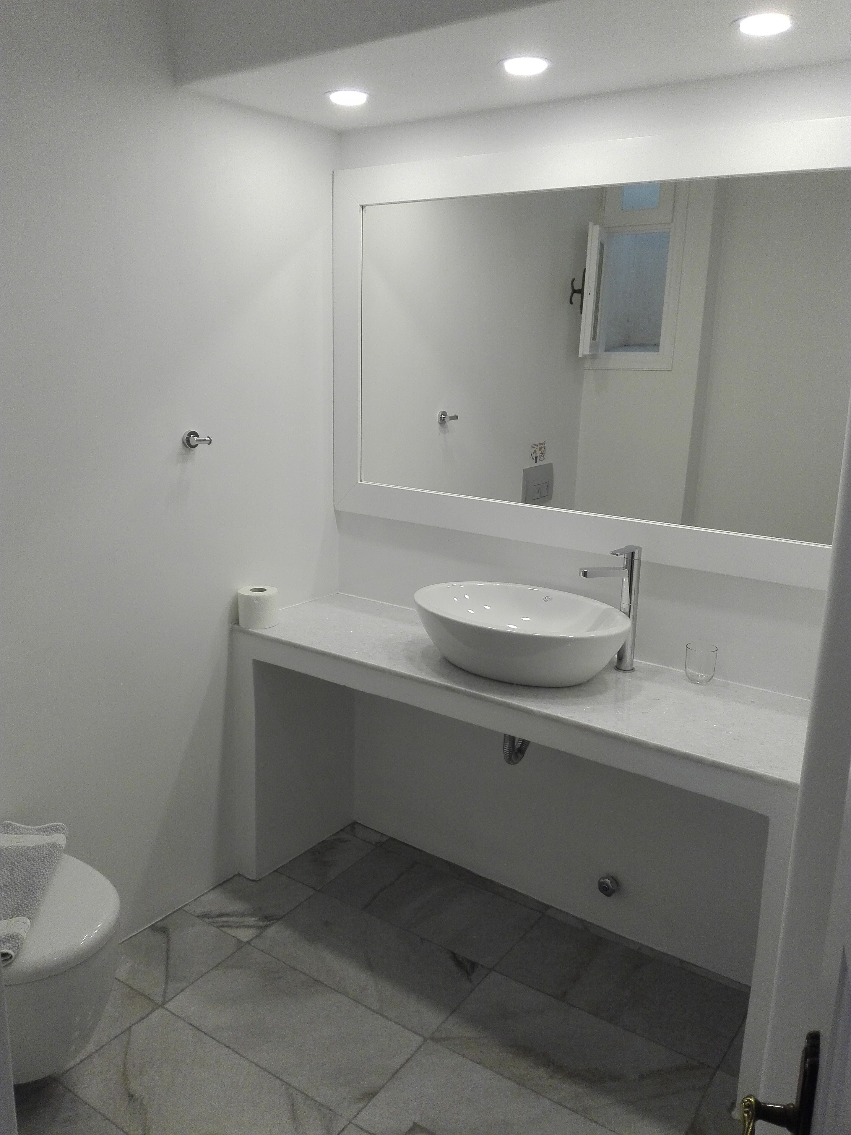 Un baño moderno con lavamanos, espejo y retrete blancos.
