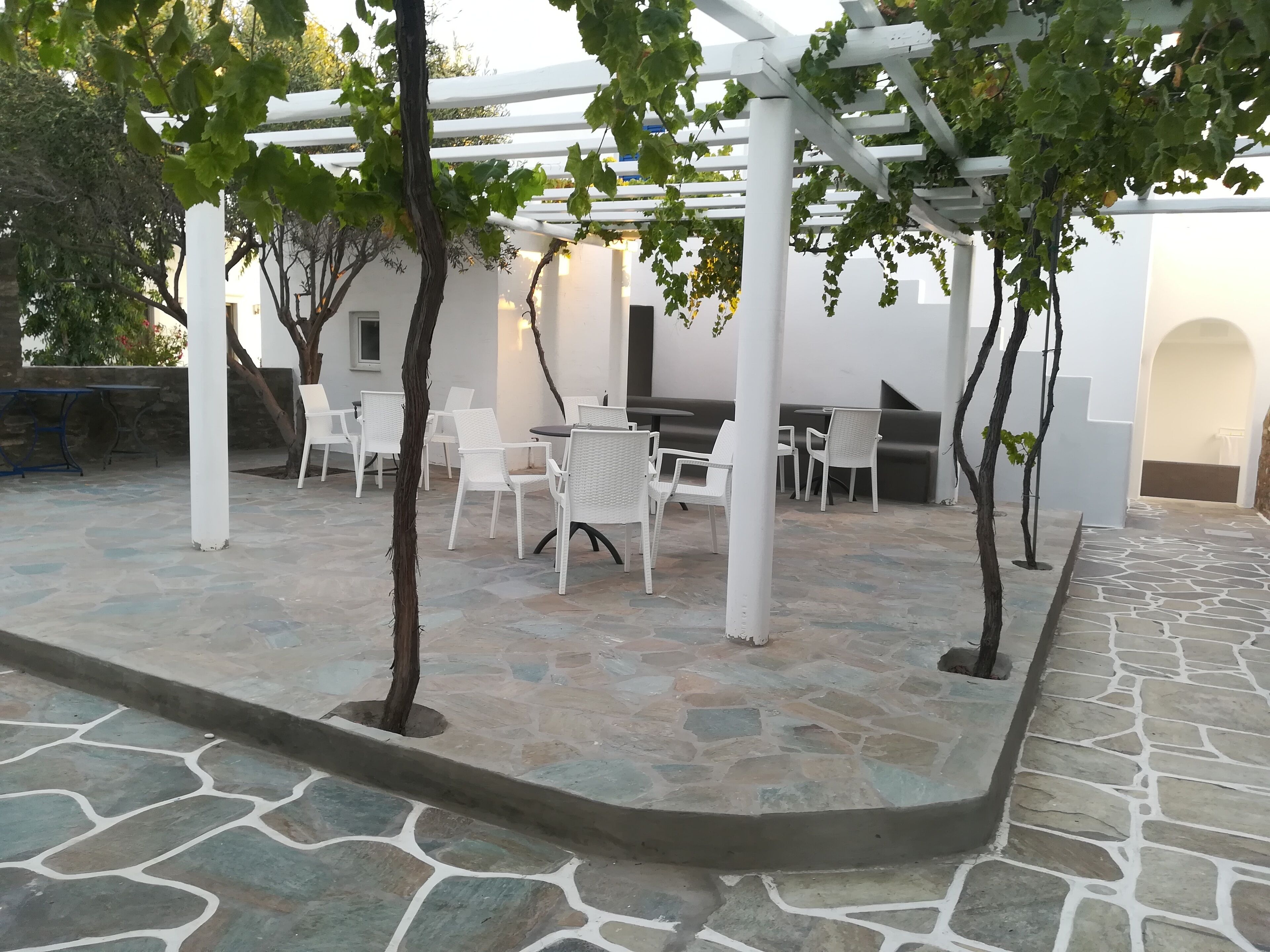 A patio area with stone flooring, white furniture, and a pergola structure.