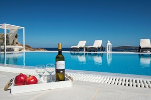 A poolside setting with a bottle of wine, glasses, and pomegranates on a tray. - Villa Irini (Paros)