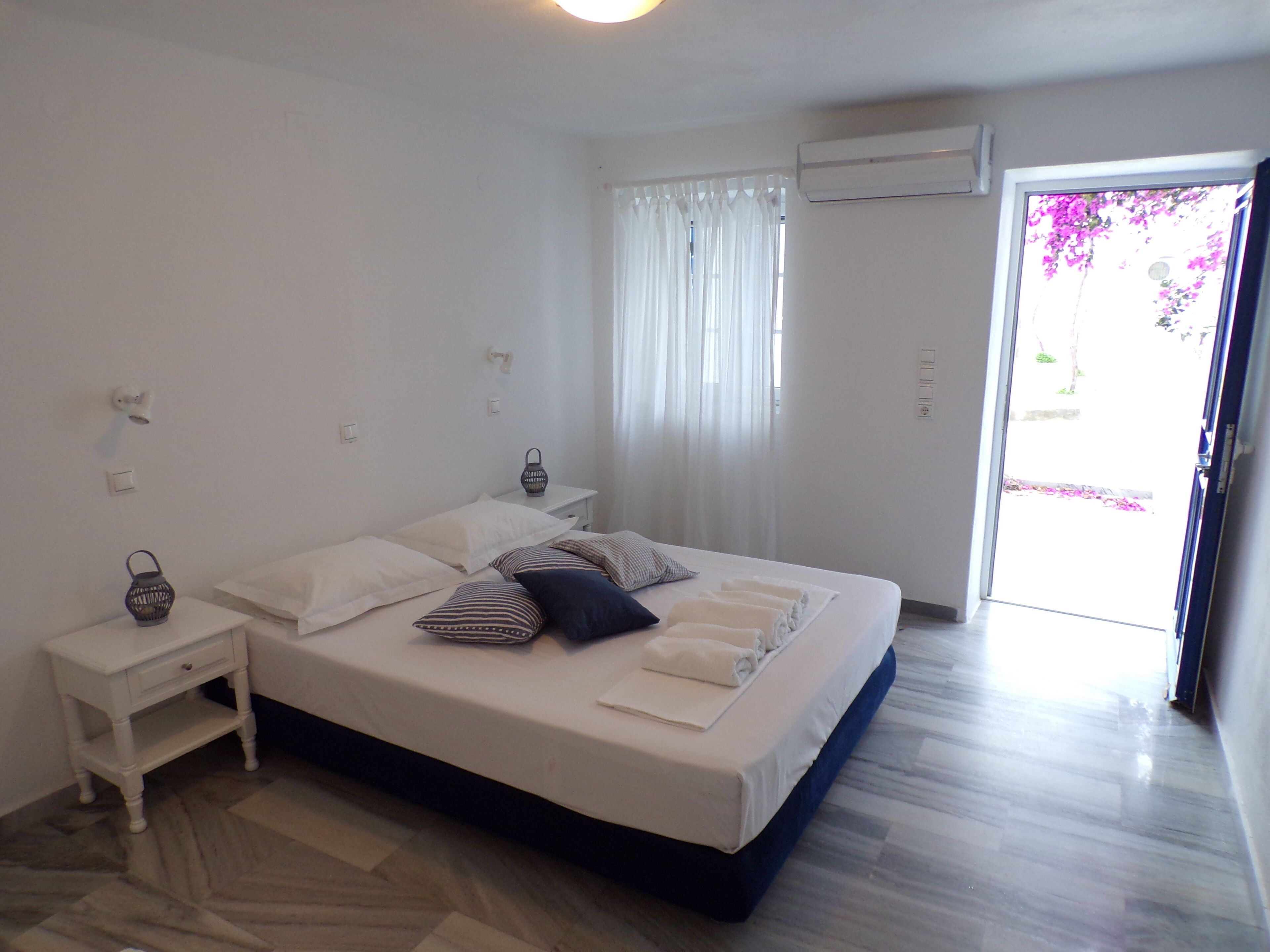 Quarto com cama, mesas de cabeceira, ar condicionado e vista para o exterior.