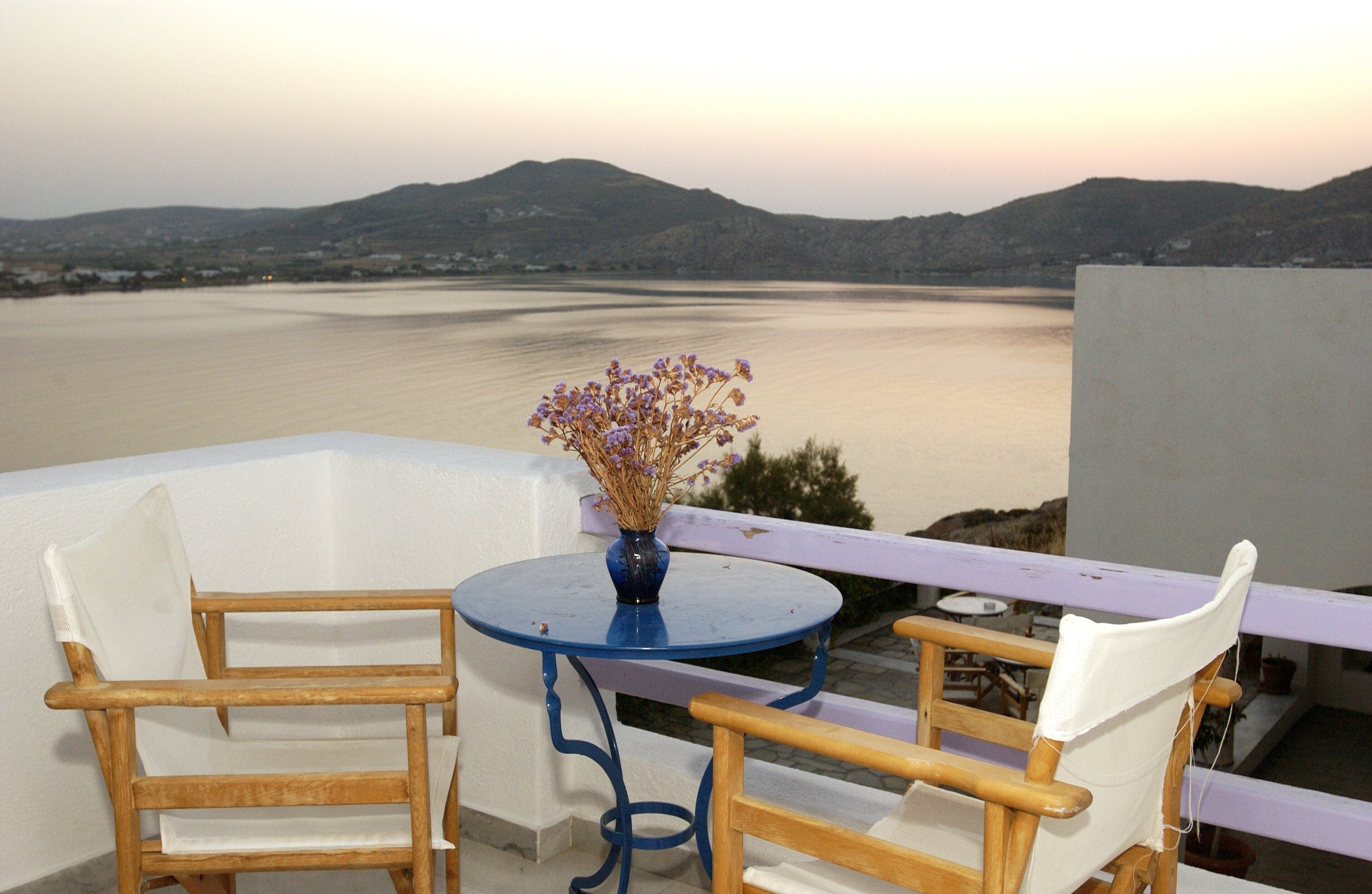 A balcony with a table and chairs, overlooking a body of water and distant hills.