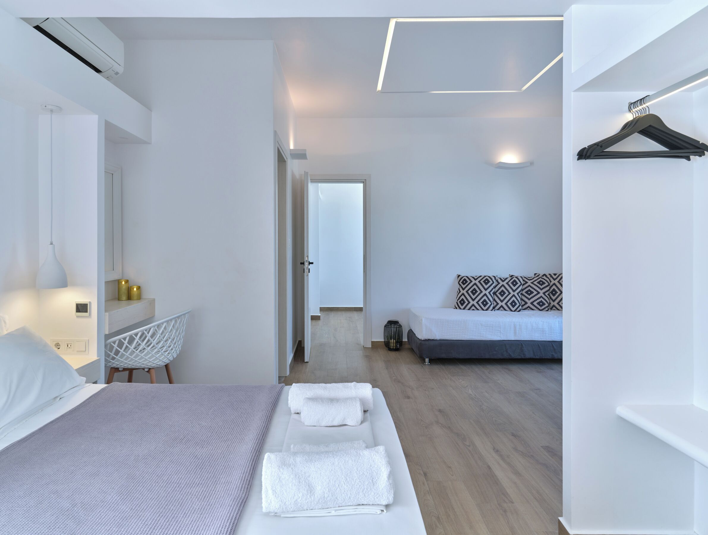 A modern hotel room with a bed, bedside table, and a chair. There is a door leading to another room.