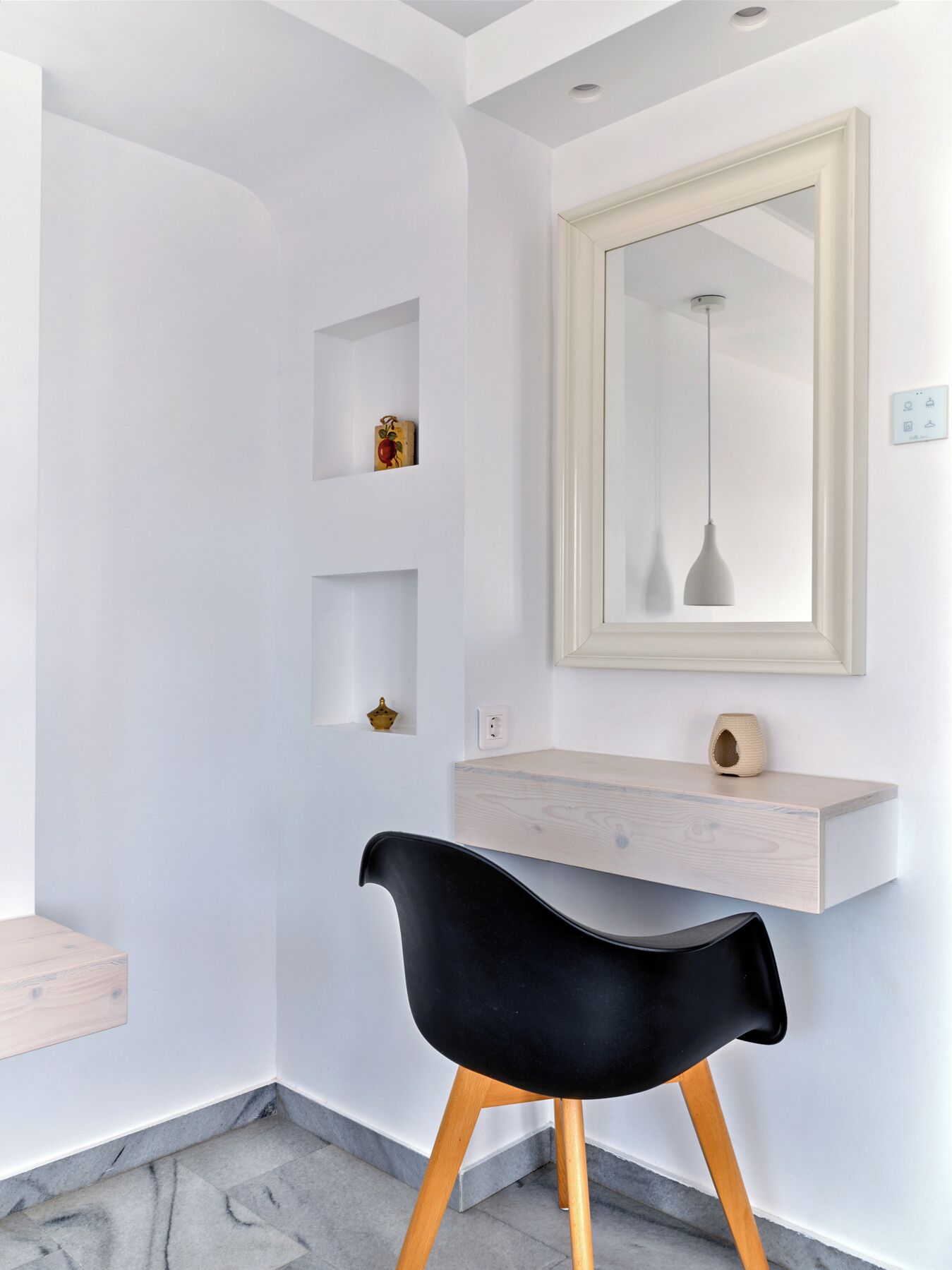 A modern bathroom with a white vanity, a black chair, and a mirror with a pendant light.