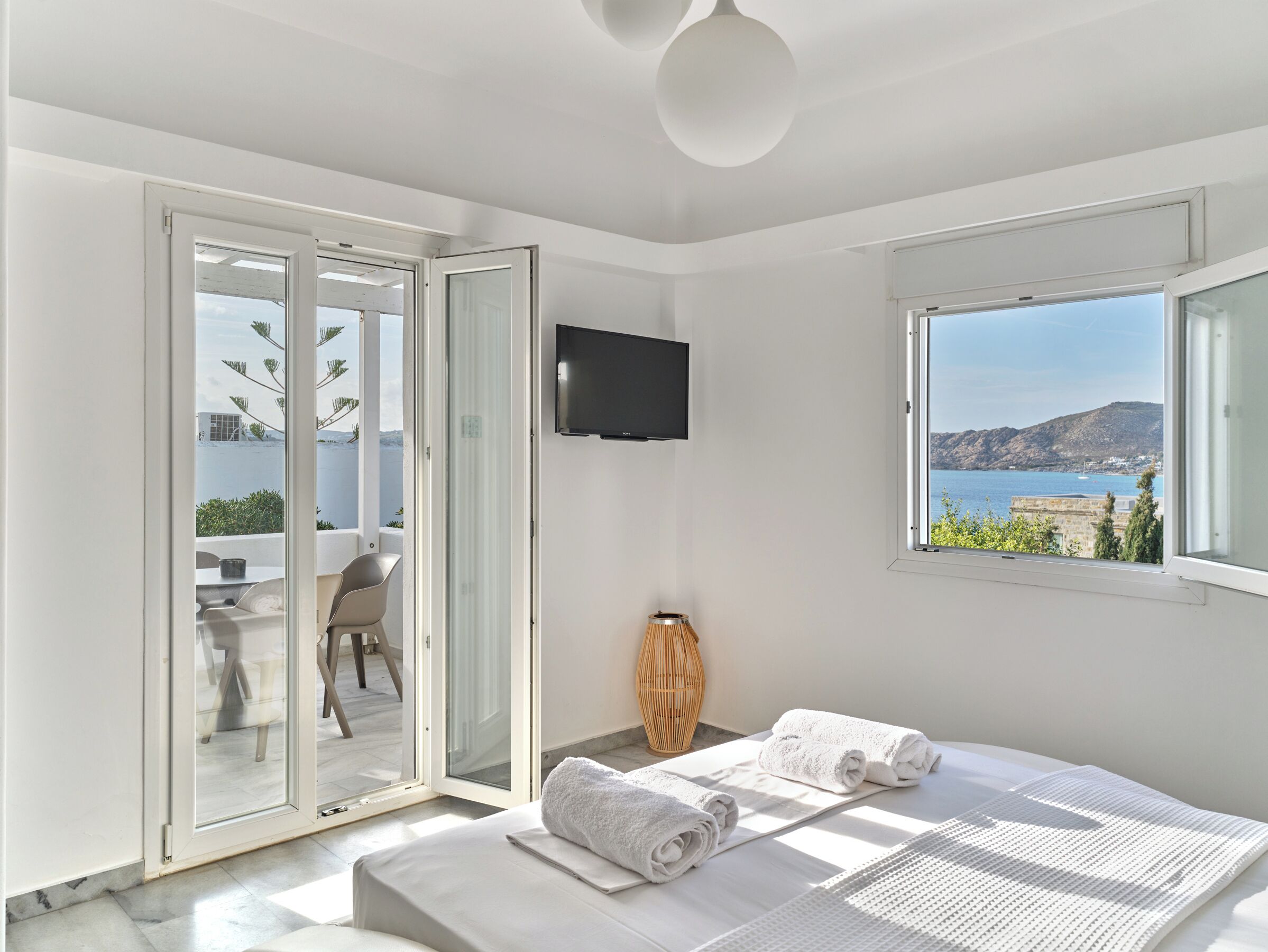 Een moderne slaapkamer met een bed, een televisie, uitzicht op zee en een balkon met een stoel en tafel.