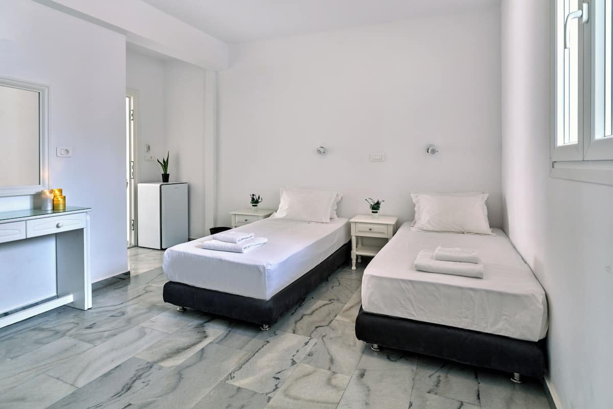 A modern hotel room with two beds, a desk, and a small kitchenette.