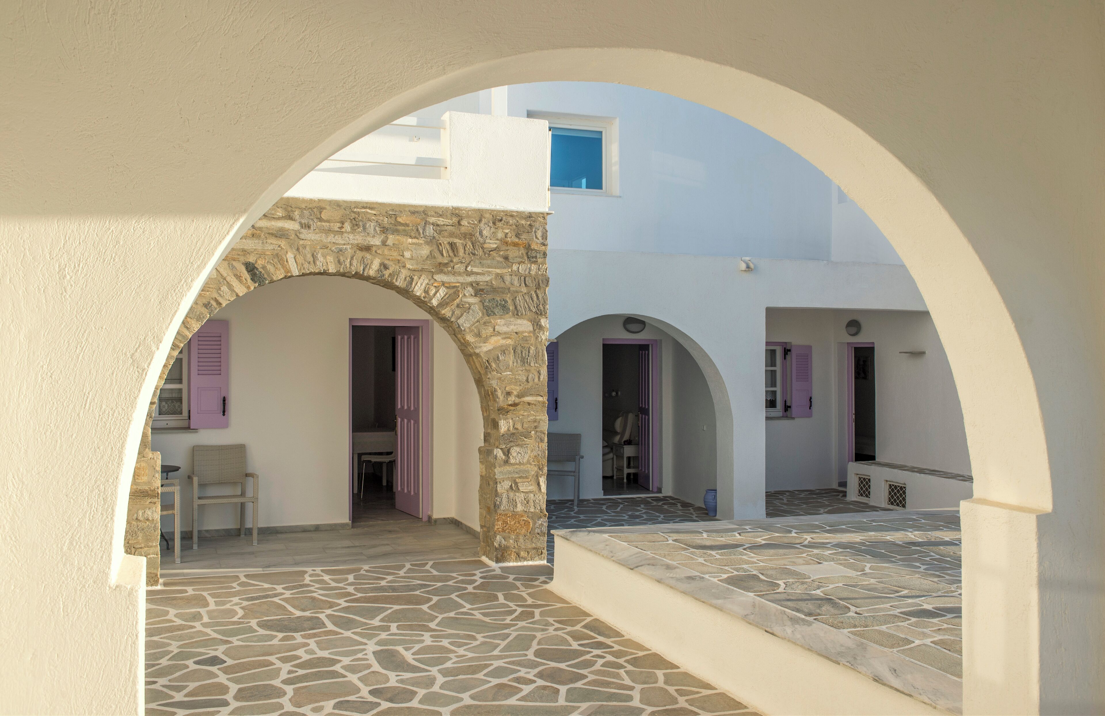 An architectural view of a building with stone and white walls, featuring arched doorways and a stone-paved courtyard.