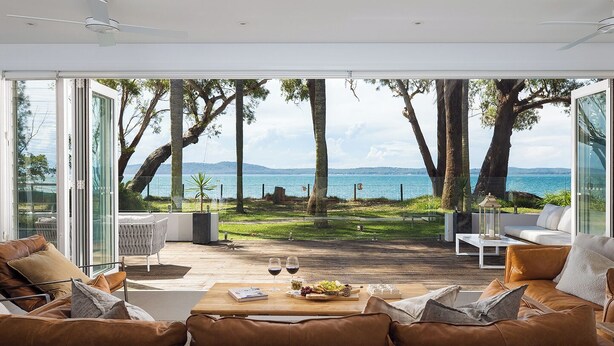 A modern living room with a view of the sea, furnished with leather sofas and a wooden coffee table. - Azure Haven – A Waterfront Luxury Retreat for Families (Corlette)
