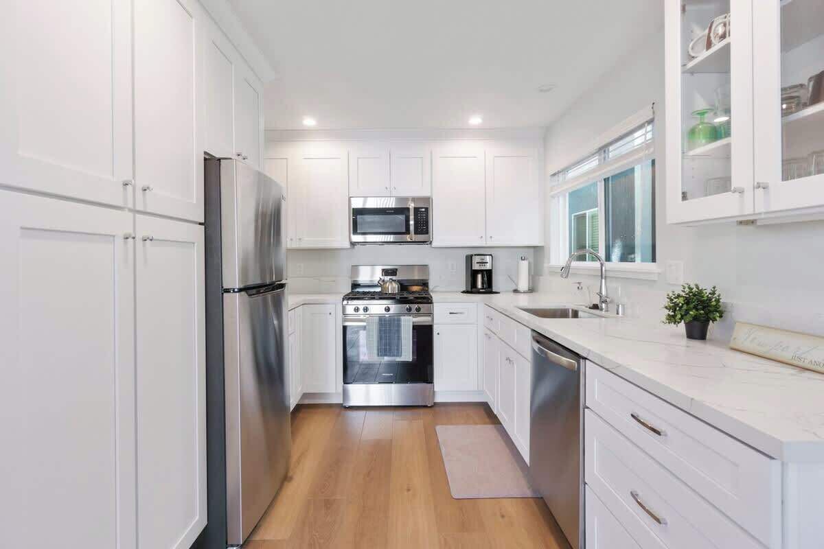 A modern kitchen with white cabinets, stainless steel appliances, and a wooden floor.