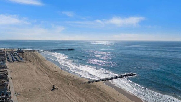 A beach with a pier extending into the ocean, sandy beach, and a clear sky.