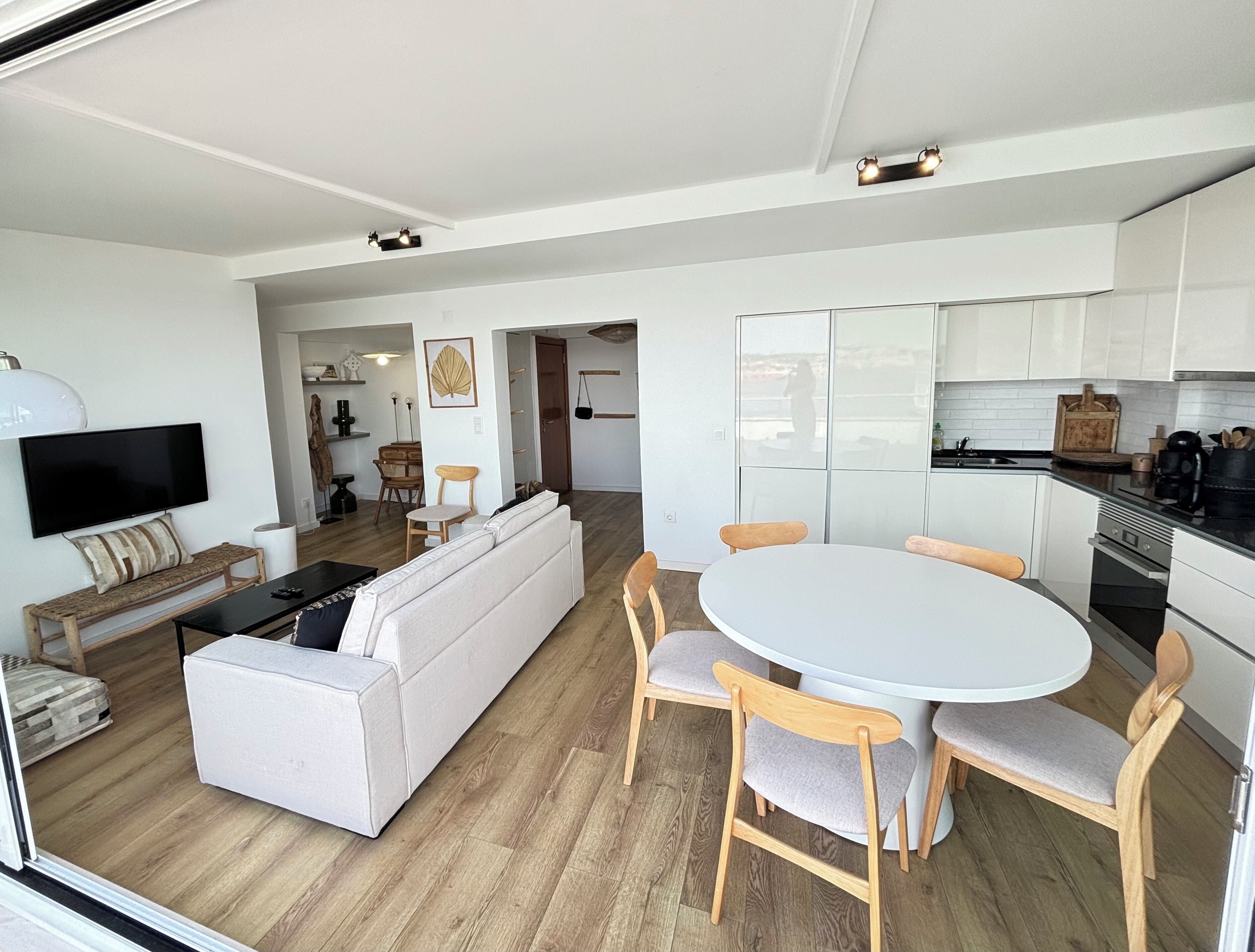 A modern living room with a sofa, TV, and dining area with chairs and a table.