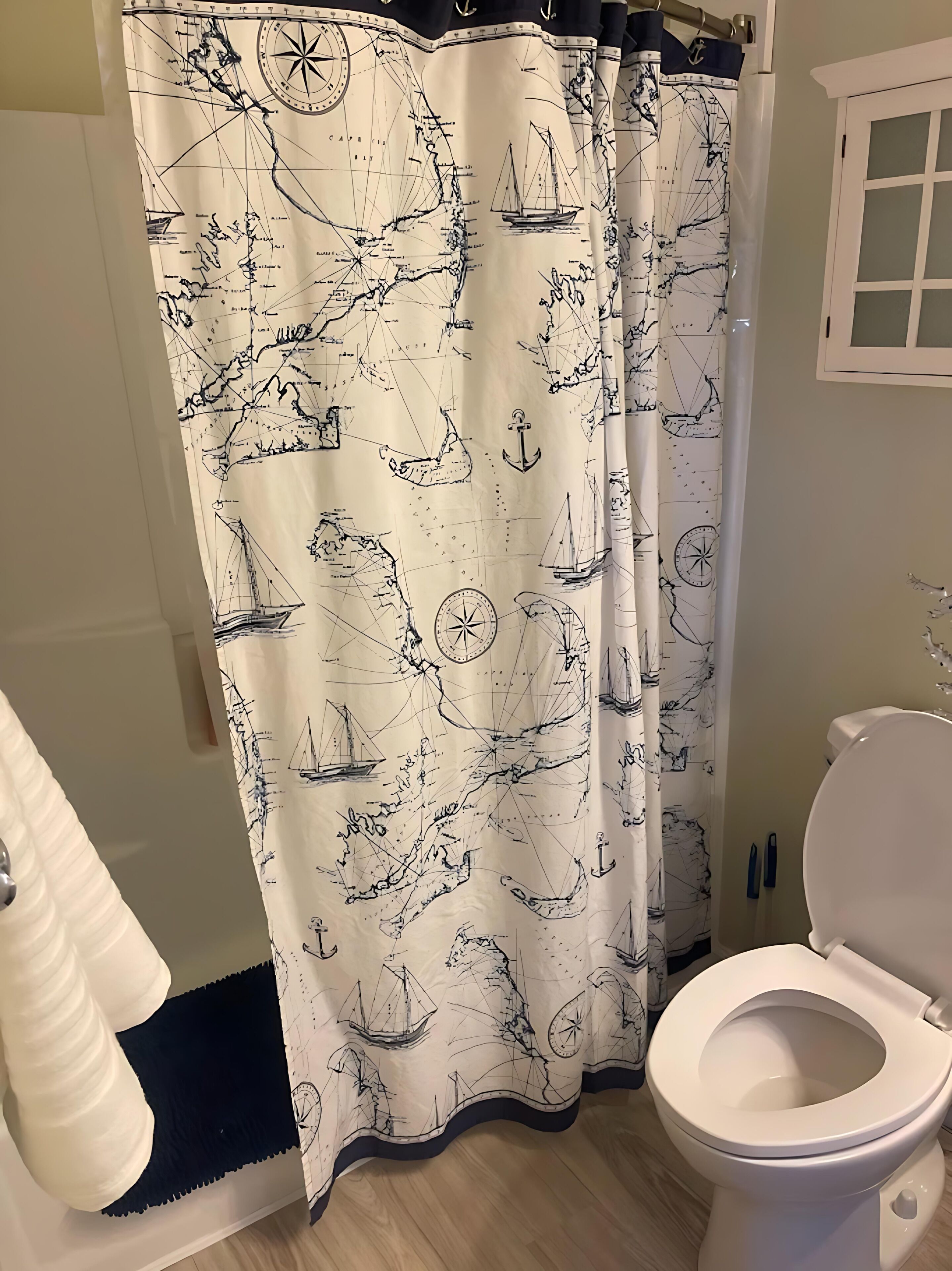 A bathroom with a nautical-themed shower curtain, a white toilet, and a wooden floor.