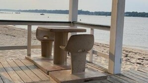 A wooden deck with a table and chairs, overlooking a beach and water. - River Retreat  On The Toms River (Ocean Gate)