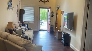 A spacious living room with a high ceiling, a ceiling fan, a large window, and a door leading to the outside. - River Retreat  On The Toms River (Ocean Gate)