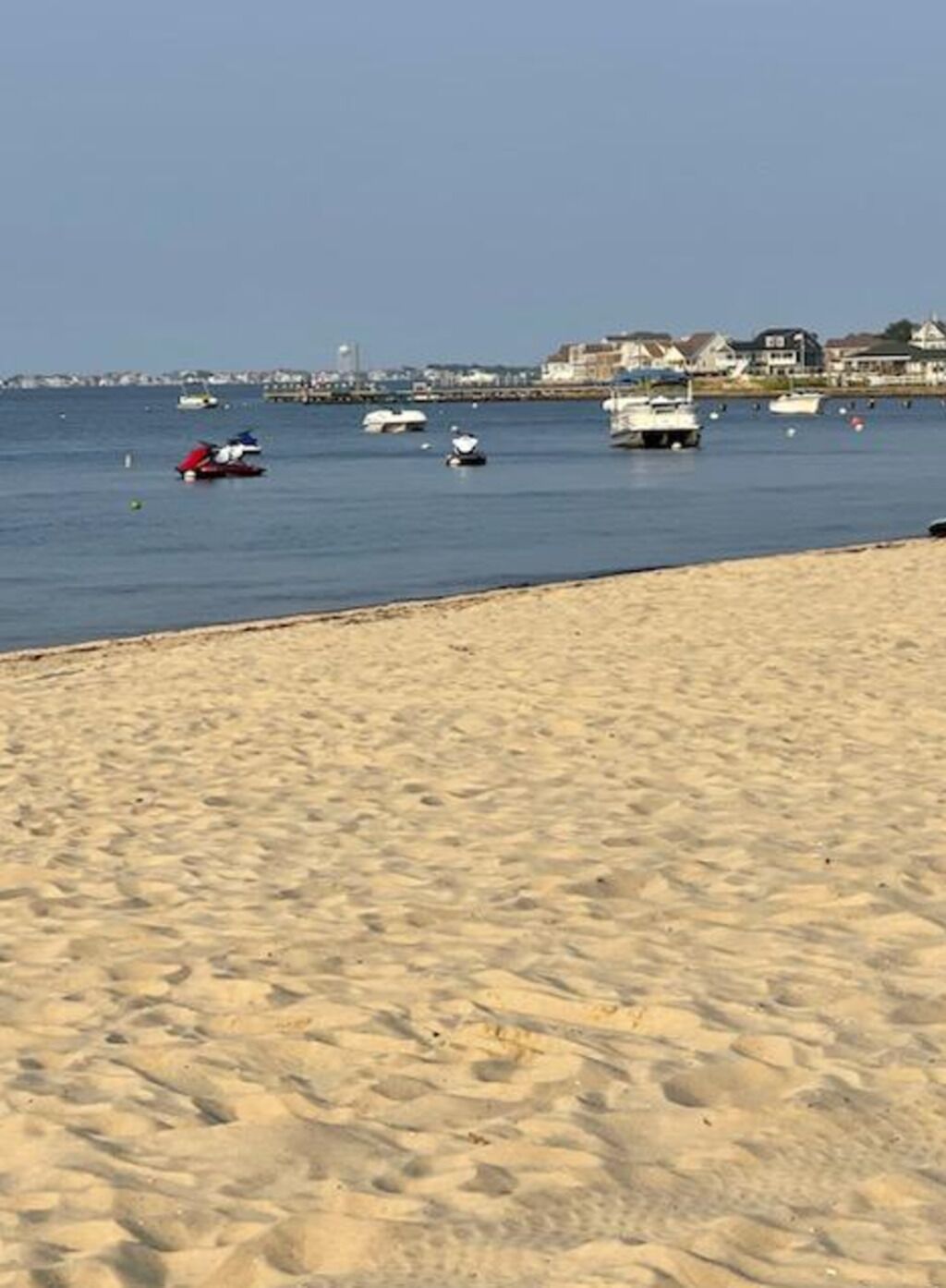 Ein Sandstrand mit Booten im Wasser und Häusern im Hintergrund.