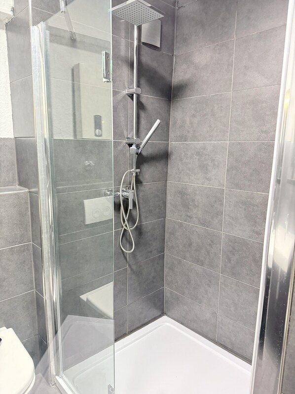 A modern shower area with a glass door, a handheld showerhead, and a wall-mounted control panel.