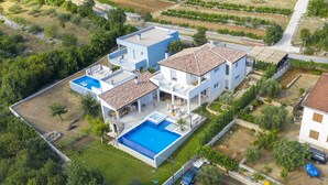 Une maison moderne à deux étages, dotée d’une grande piscine, d’un patio couvert et d’un jardin.
