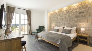 Une chambre avec un mur en pierre, un lit avec une literie grise, un bureau avec une chaise et une vue par une fenêtre ornée de rideaux.