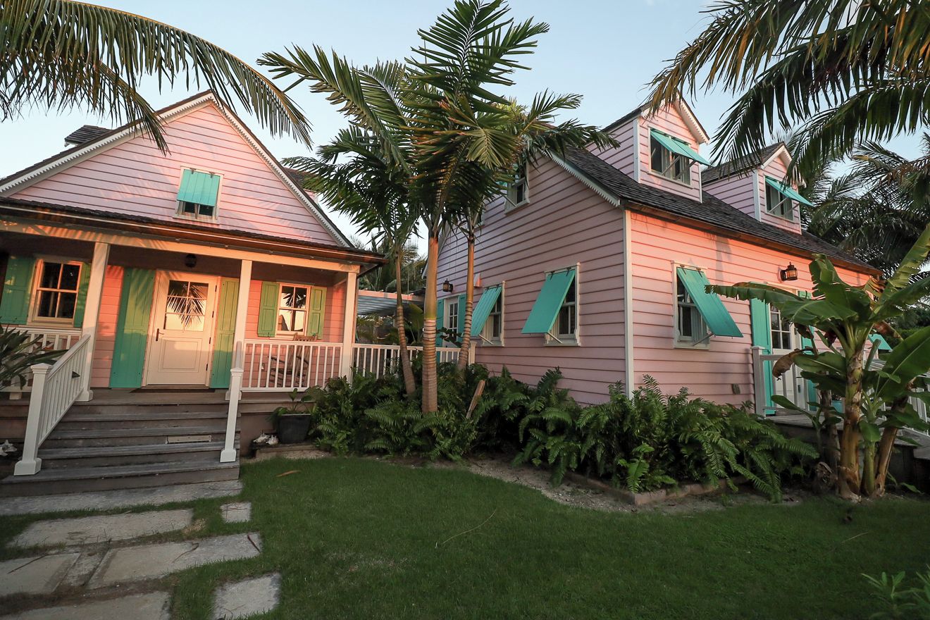 A pink house with a porch, green shutters, and a stone staircase leading to the front door.