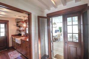 A wooden kitchen with a built-in sink and shelves, a wooden door leading to an outdoor deck with a table and chairs.