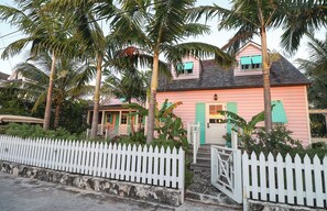 A pink house with a white picket fence, surrounded by palm trees.