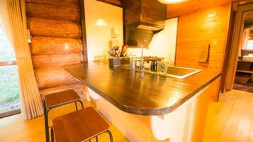 A wooden cabin interior with a kitchen area featuring a bar counter, stools, and a sink.