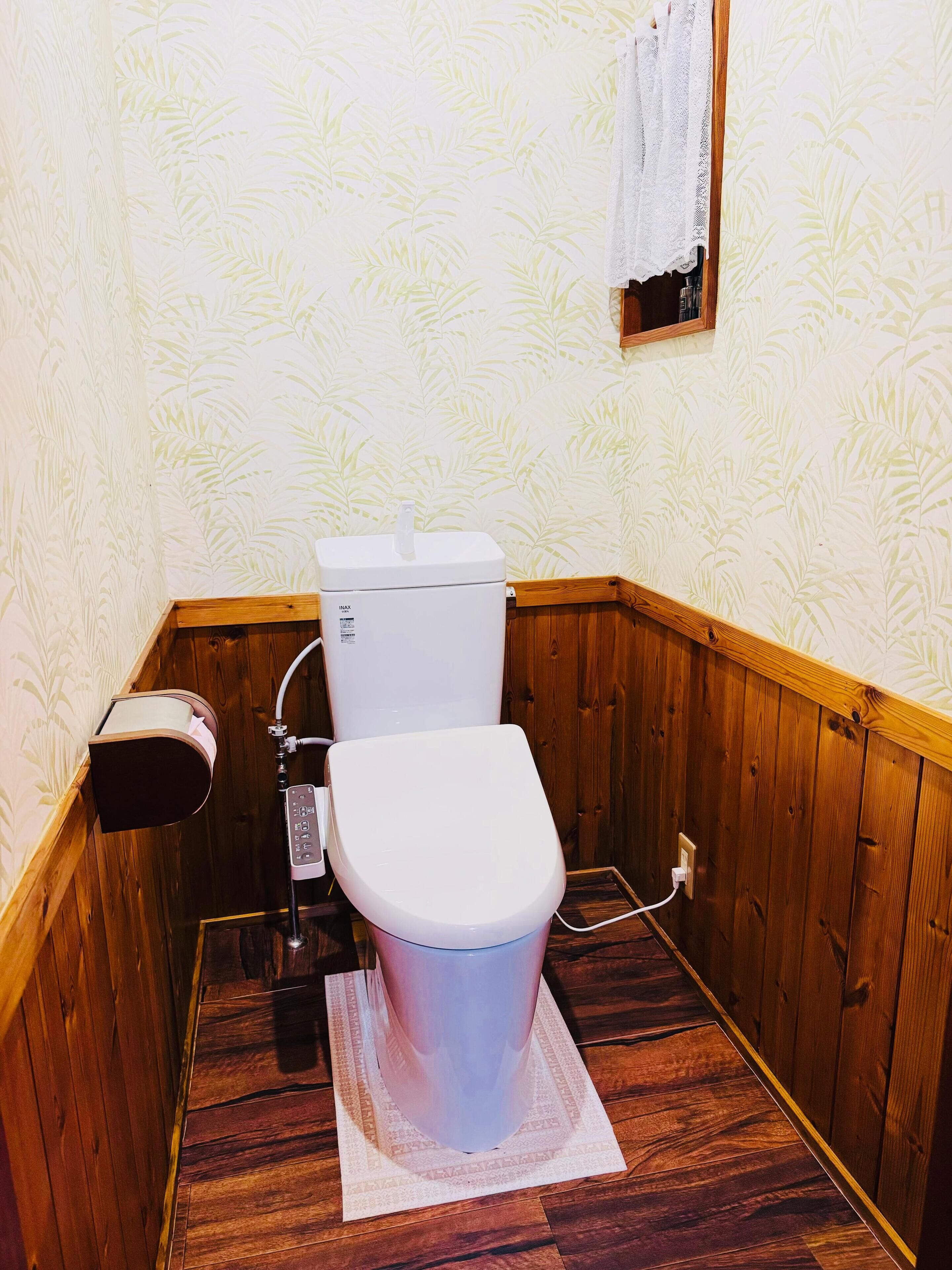 A small, wooden-paneled bathroom with a toilet, a paper towel dispenser, and a wall-mounted calendar.