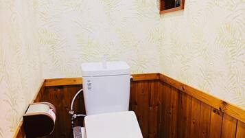 A small, wooden-paneled bathroom with a toilet, a paper towel dispenser, and a wall-mounted calendar.