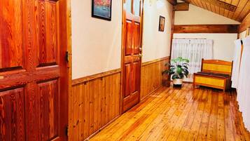 A wooden hallway with a wooden door, a framed picture on the wall, and a bench in the distance.