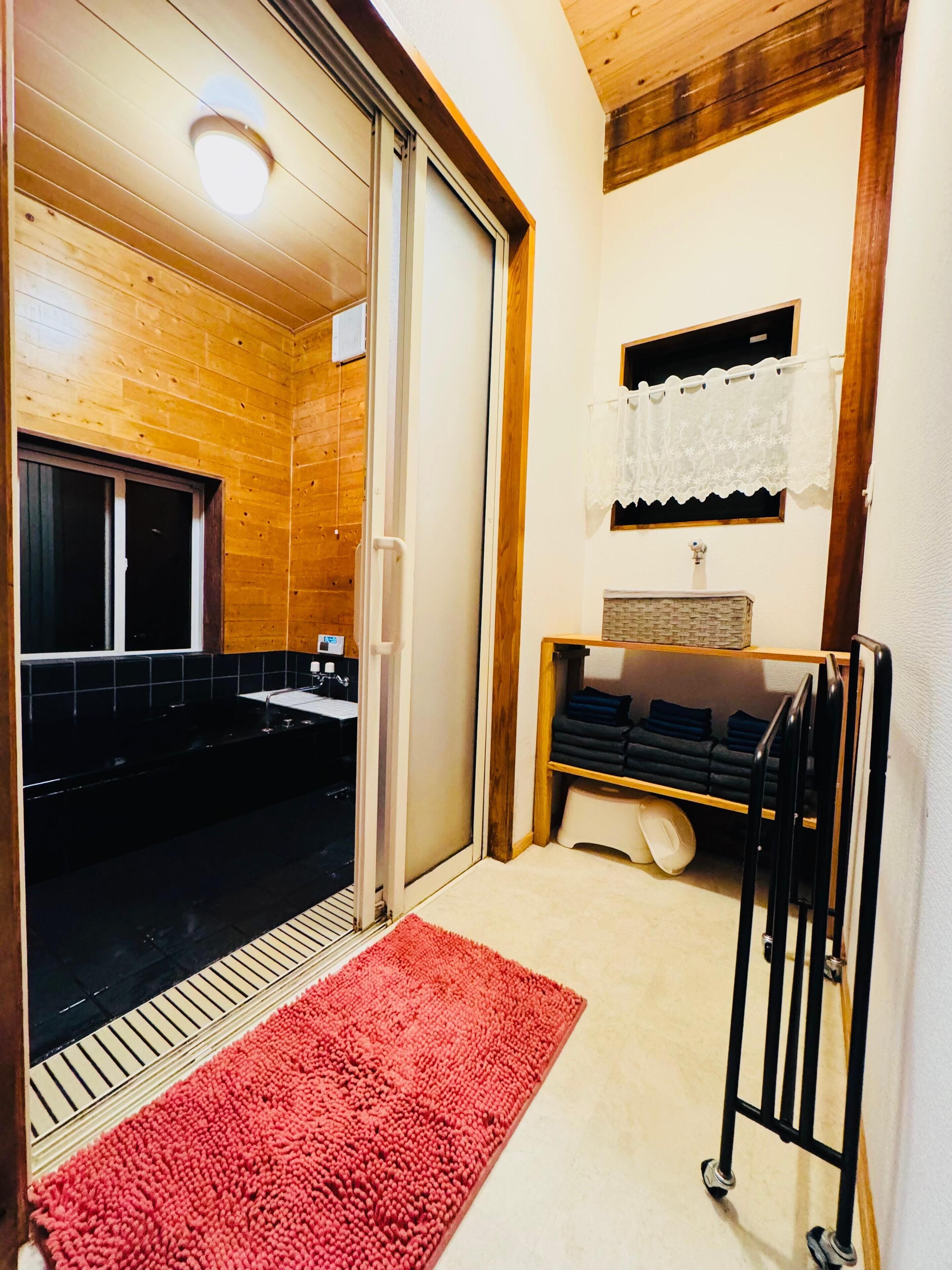 A bathroom with a wooden interior, a black bathtub, a white sink, and a red rug.