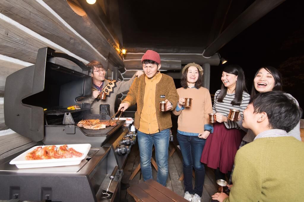 A group of people around a barbecue grill with pizza and drinks.